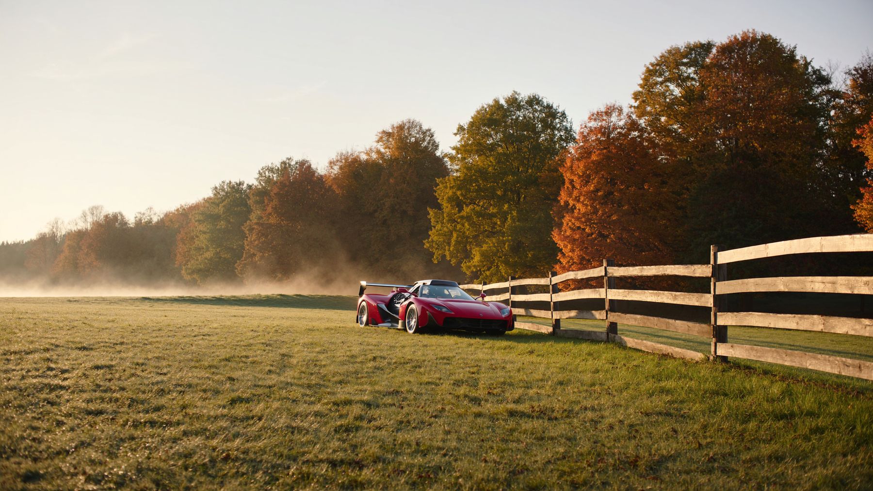 A scarlet supercar on pasture grass at sunrise beside a ranch fence